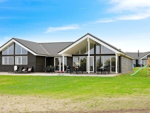 A modern two-story building with a covered patio area, large windows, and a play structure in the yard. - 5 Star Holiday Home in Bogense (Bogense)