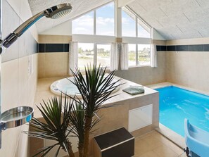 A modern bathroom with a bathtub, a shower, and a window overlooking a pool. - 5 Star Holiday Home in Bogense (Bogense)