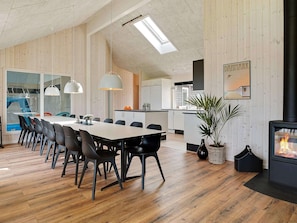 A modern kitchen with wooden walls, a dining area with a long table and chairs, and a fireplace. - 5 Star Holiday Home in Bogense (Bogense)