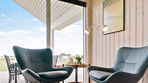 Ein Zimmer mit zwei modernen Stühlen, einem kleinen Tisch mit einer Vase und einem großen Fenster mit Blick ins Freie.