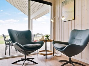 A room with two modern chairs, a small table with a vase, and a large window offering a view of the outdoors. - 5 Star Holiday Home in Bogense (Bogense)