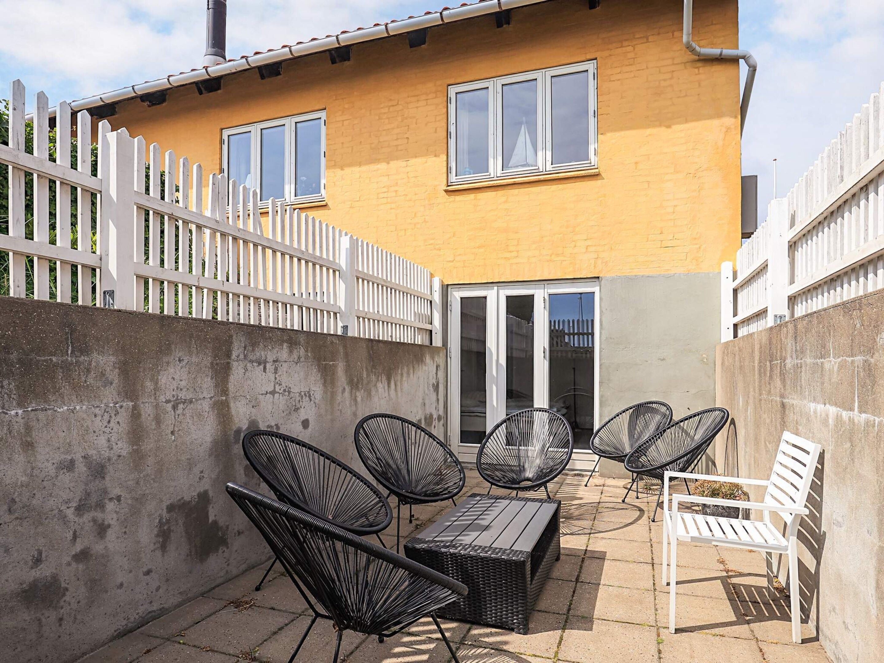 Ein zweistöckiges Haus mit einer Terrasse und Gartenmöbeln.