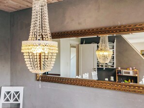 Un lustre doté d’une armature dorée et de décorations en cristal, suspendu au-dessus d’un miroir encadré d’une armature dorée ornée.