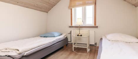 Una habitación pequeña y acogedora con dos camas individuales, un radiador y una ventana con persiana.
