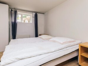 Une chambre à coucher avec un lit, une fenêtre avec des rideaux, un radiateur et une étagère en bois.