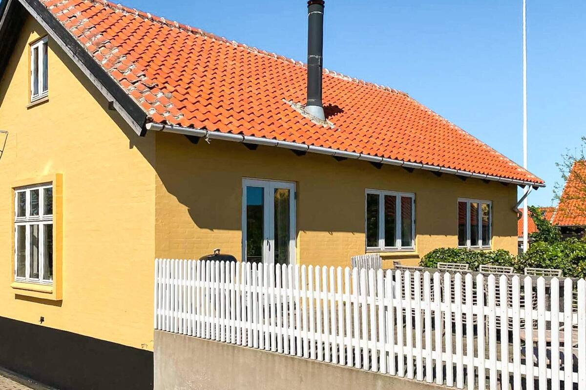 Un edificio amarillo con techo de tejas rojas, ventanas blancas y valla de piquetes blancos.