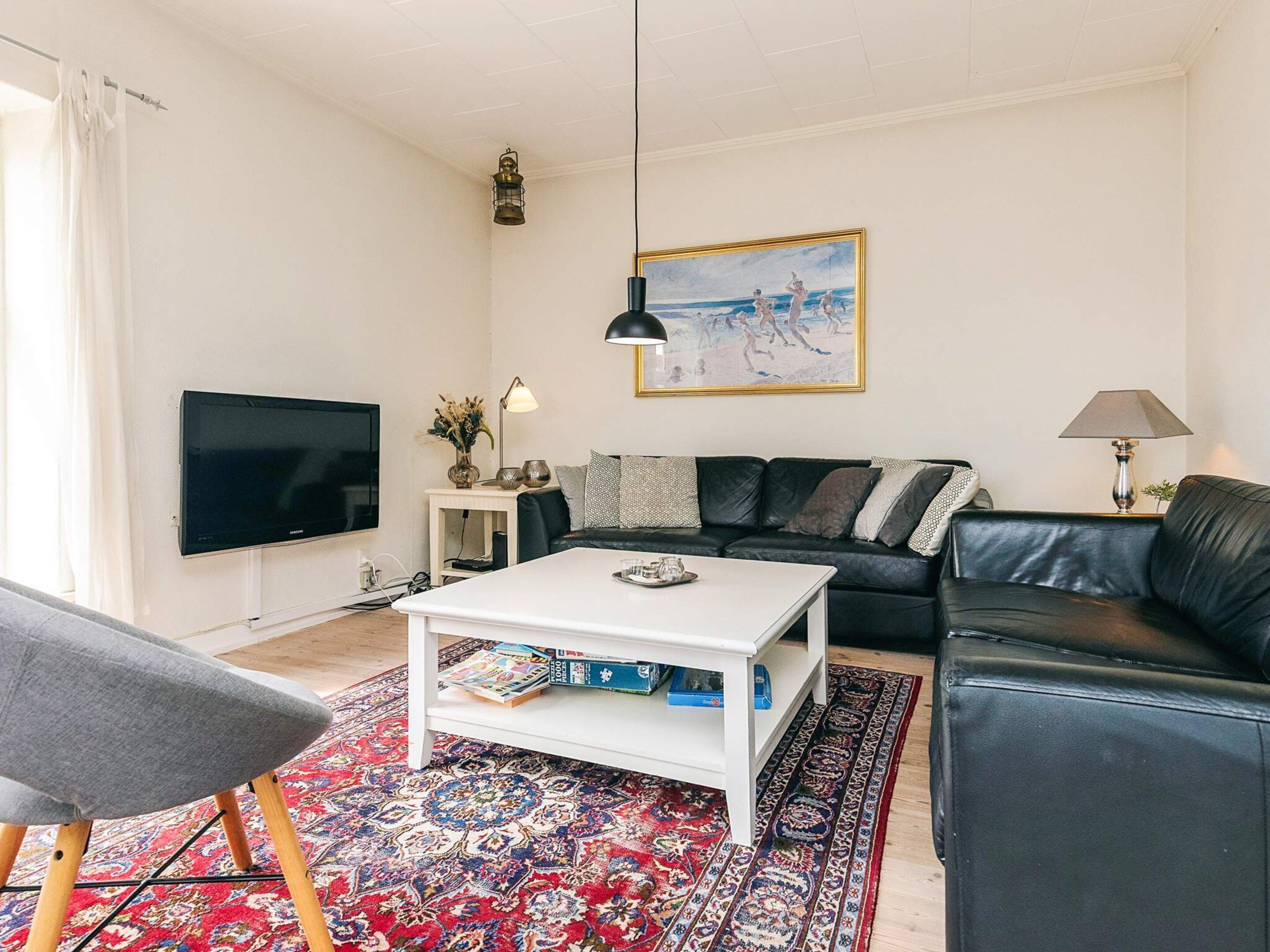 Ein modernes Wohnzimmer mit einer schwarzen Ledersofa, einem weißen Couchtisch, einem Flachbildfernseher und einem gemusterten Teppich.