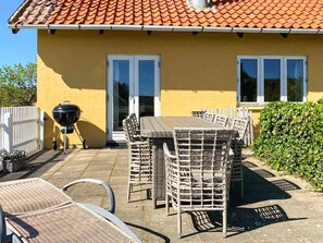 A yellow building with a tiled roof, a patio with wicker furniture, and a barbecue grill. - Balmy Holiday Home in Skagen near Sea (Skagen)