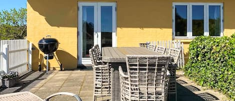Une terrasse avec une table et des chaises, un barbecue et une clôture blanche.