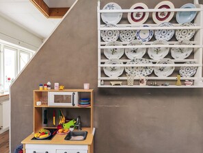 Une cuisine avec un comptoir en bois, un évier et un four à micro-ondes. On y trouve une étagère avec différentes assiettes et une petite étagère avec des ustensiles de cuisine et un vase jaune.