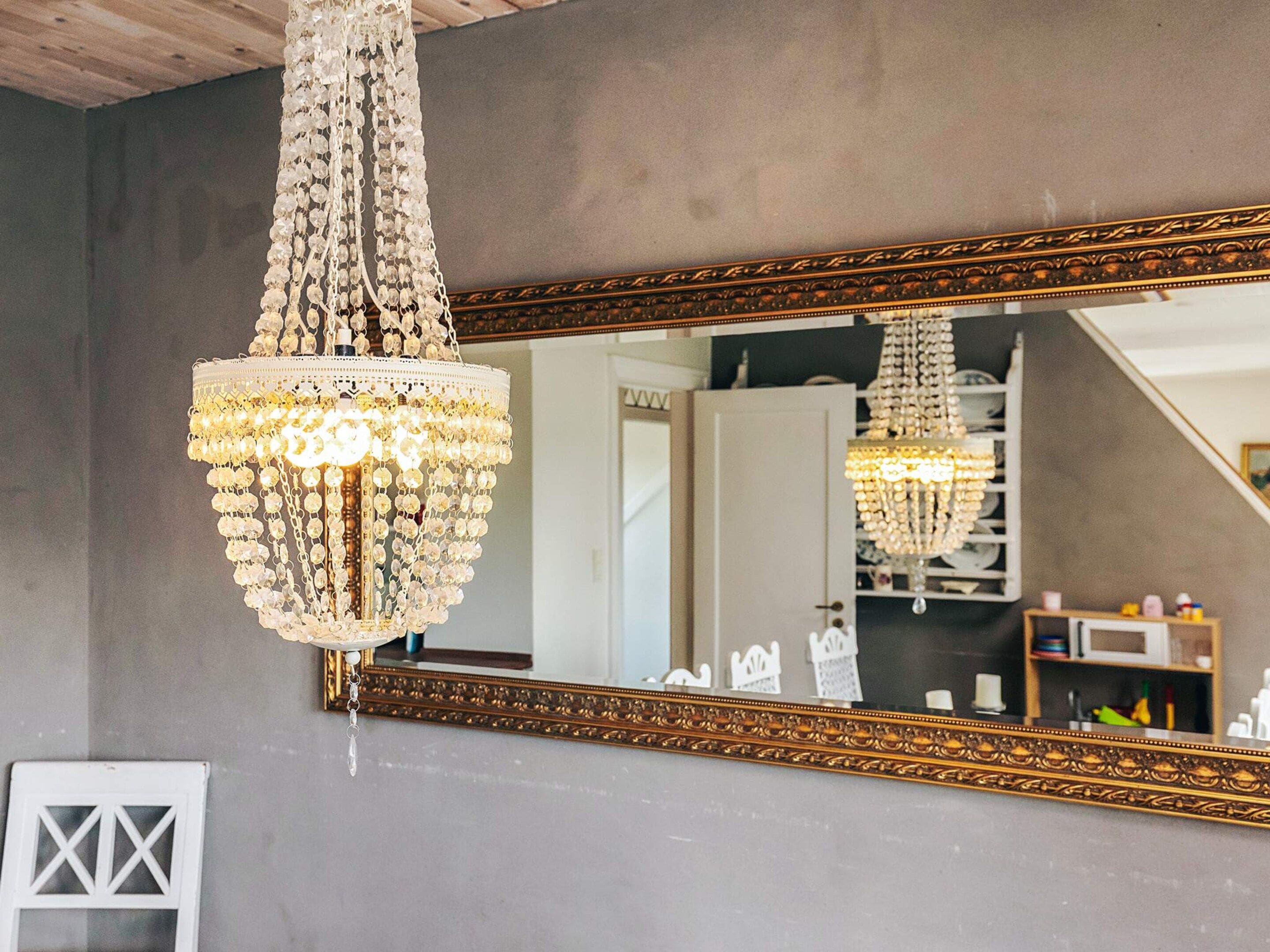 Un lampadario con diversi livelli di cristalli sospeso al soffitto, un ampio specchio decorativo con cornice dorata e una porta bianca sullo sfondo.