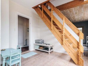 Una habitación con escalera de madera, una puerta blanca, un sillón azul, una mesita pequeña y un armario blanco.