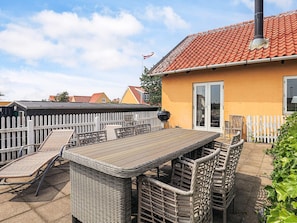 Une terrasse avec une table et des chaises, un barbecue et une clôture blanche en bois.
