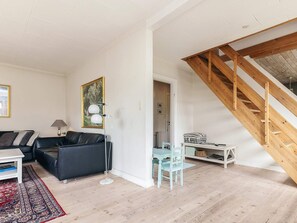 A modern living room with a black leather sofa, a white coffee table, a floor lamp, and a blue chair. A staircase with wooden railings leads to an upper level.
