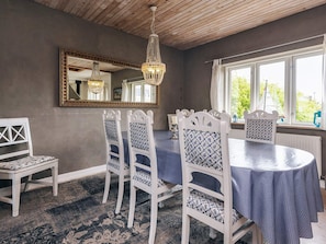 Un coin repas avec une table ronde, des chaises blanches, un tapis à motifs, un lustre et une fenêtre donnant sur un paysage verdoyant.