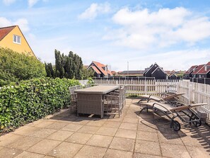 Un espace patio aménagé avec une table et des chaises, un banc en bois et une clôture blanche à lattes.