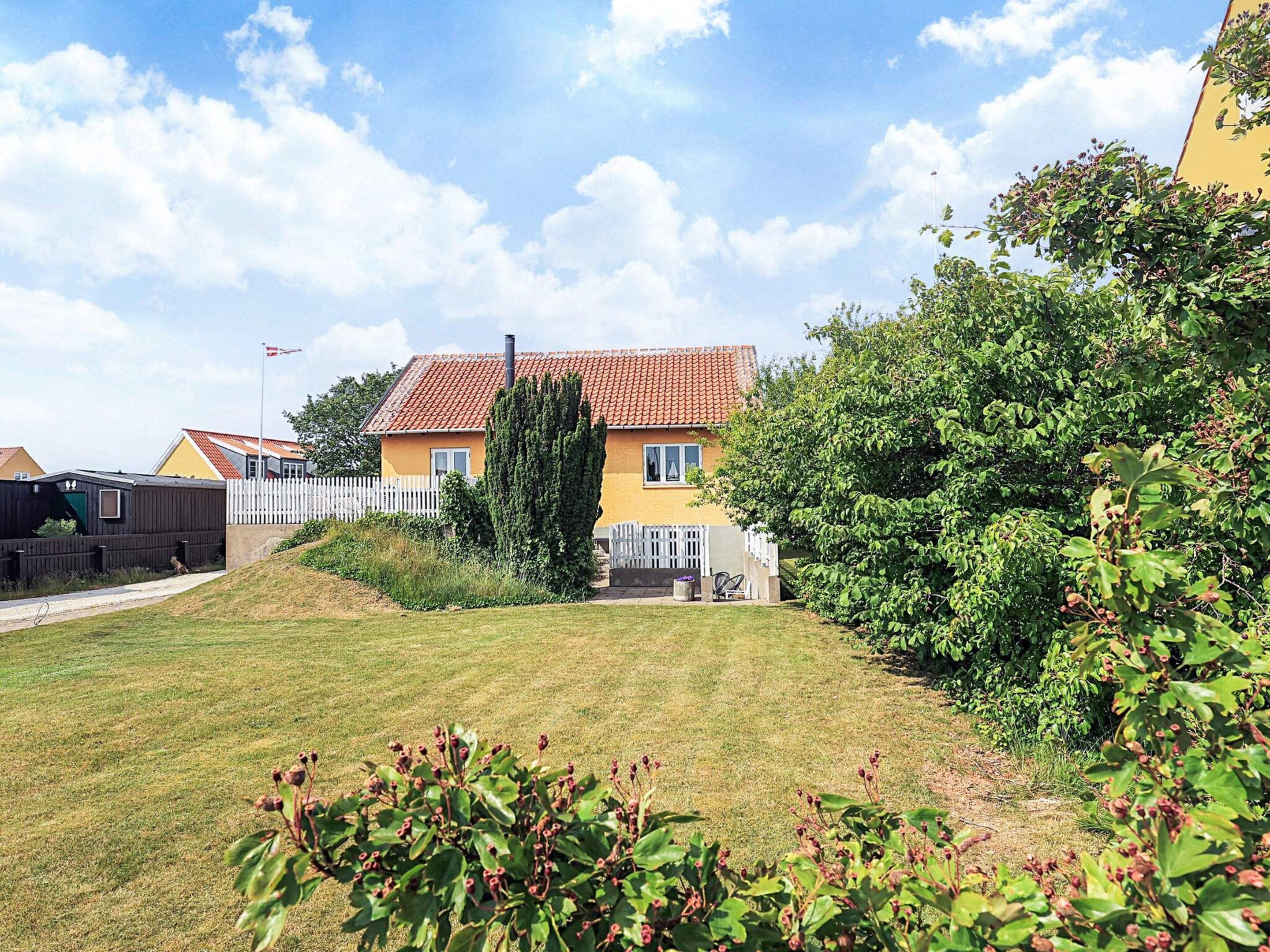 A residential house with a red-tiled roof, a white picket fence, and a well-maintained lawn.