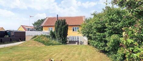 A residential house with a red-tiled roof, a white picket fence, and a well-maintained lawn.
