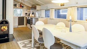 Une cuisine moderne dotée d’un poêle à bois, de meubles blancs et d’un coin repas avec une table et des chaises blanches.