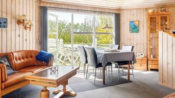 Una habitación con techo de madera, un sofá de cuero marrón, una mesa de comedor con sillas y un mueble de madera.