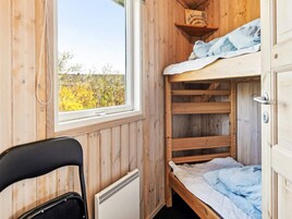Una habitación de cabaña de madera con una litera, una silla y una ventana con vistas a un paisaje natural.