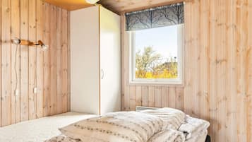 A wooden-paneled room with a bed, a wardrobe, and a window with a view of trees.