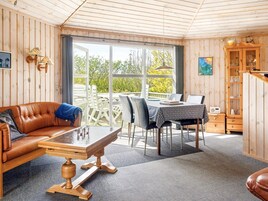 Una habitación acogedora con detalles de madera, un sofá de cuero, una mesa de comedor con sillas y un aparador con cristalería.