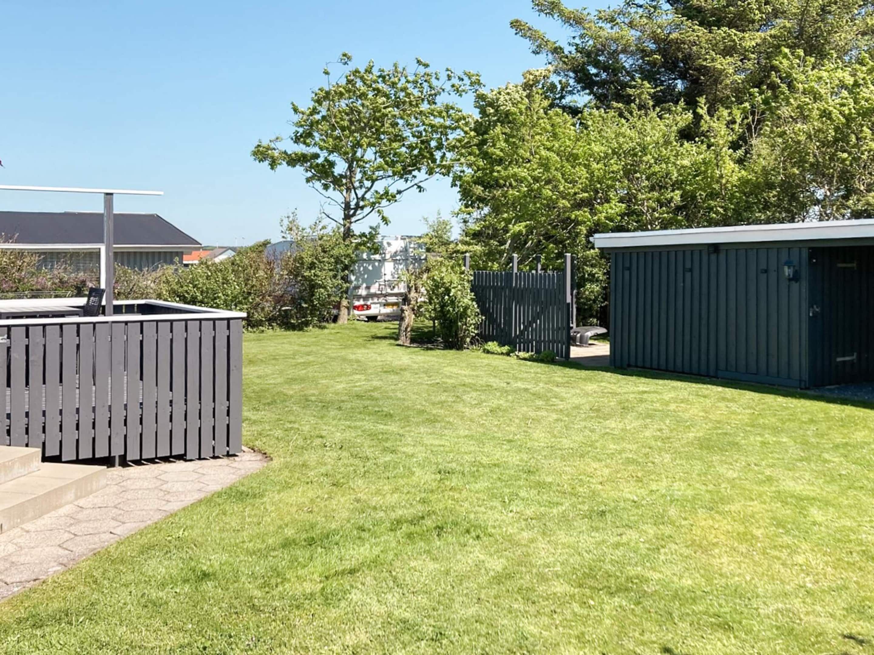 A well-maintained grassy yard with a metal fence, a shed, and a tree.