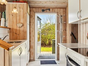 A modern kitchen with wooden accents, a built-in oven, and a view of a garden through an open door. - 4 Person Holiday Home in Vinderup (Vinderup)