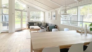 A spacious room with a large wooden dining table, white chairs, a black leather sofa, and a glass ceiling. - Adorable Holiday Home in Lolland near Sea (Rodby)