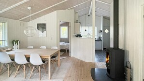 A modern interior with a dining area, a kitchen, and a wood-burning stove. - Adorable Holiday Home in Lolland near Sea (Rodby)