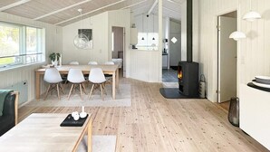 A spacious living area with a wooden floor, a dining table with chairs, a fireplace, and a kitchen in the background. - Adorable Holiday Home in Lolland near Sea (Rodby)