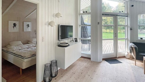 A room with a bed, a TV, a dining area, and a view of the outdoors. - Adorable Holiday Home in Lolland near Sea (Rodby)