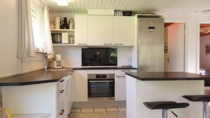 A compact kitchen with white cabinets, a built-in oven, a microwave, and a coffee maker. There are two bar stools and a patterned tile floor. - Family Fun in Ristinge - By Traum Ferienwohnungen (Sydlangeland)