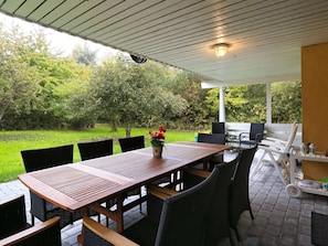 Enjoy dining or socializing in this outdoor patio area with a table and chairs, surrounded by a lush lawn and trees.