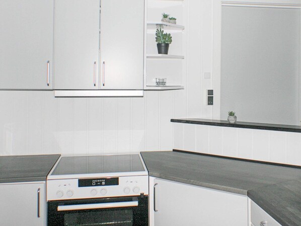 Una cocina moderna con armarios blancos, horno empotrado y encimera con una pequeña planta en maceta.