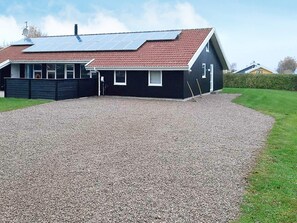 Una casa con camino de entrada de grava, paneles solares en el techo y patio cercado.