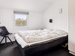 A bedroom with a bed, a chair, a window, and a wall-mounted light fixture.