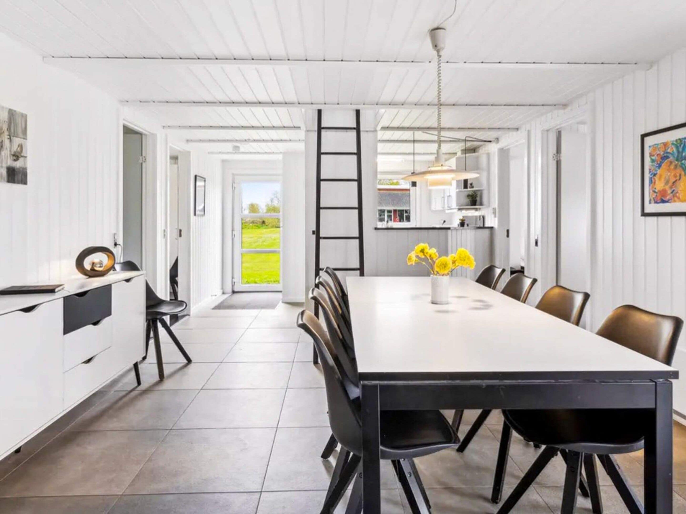 A modern kitchen with a large dining table, black chairs, and a view of the outdoors.