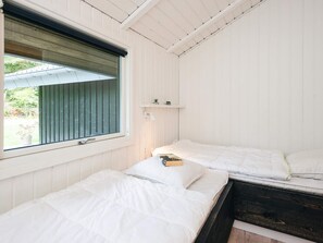 A bedroom with two beds, a window with blinds, a bedside lamp, and a small shelf with a plant. - Fascinating Holiday Home in Norre Nebel near Sea (Norre Nebel)