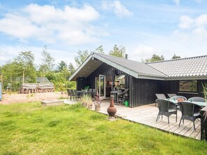 A modern outdoor dining area with a wooden deck, a large urn, and a grill. - Fascinating Holiday Home in Norre Nebel near Sea (Norre Nebel)