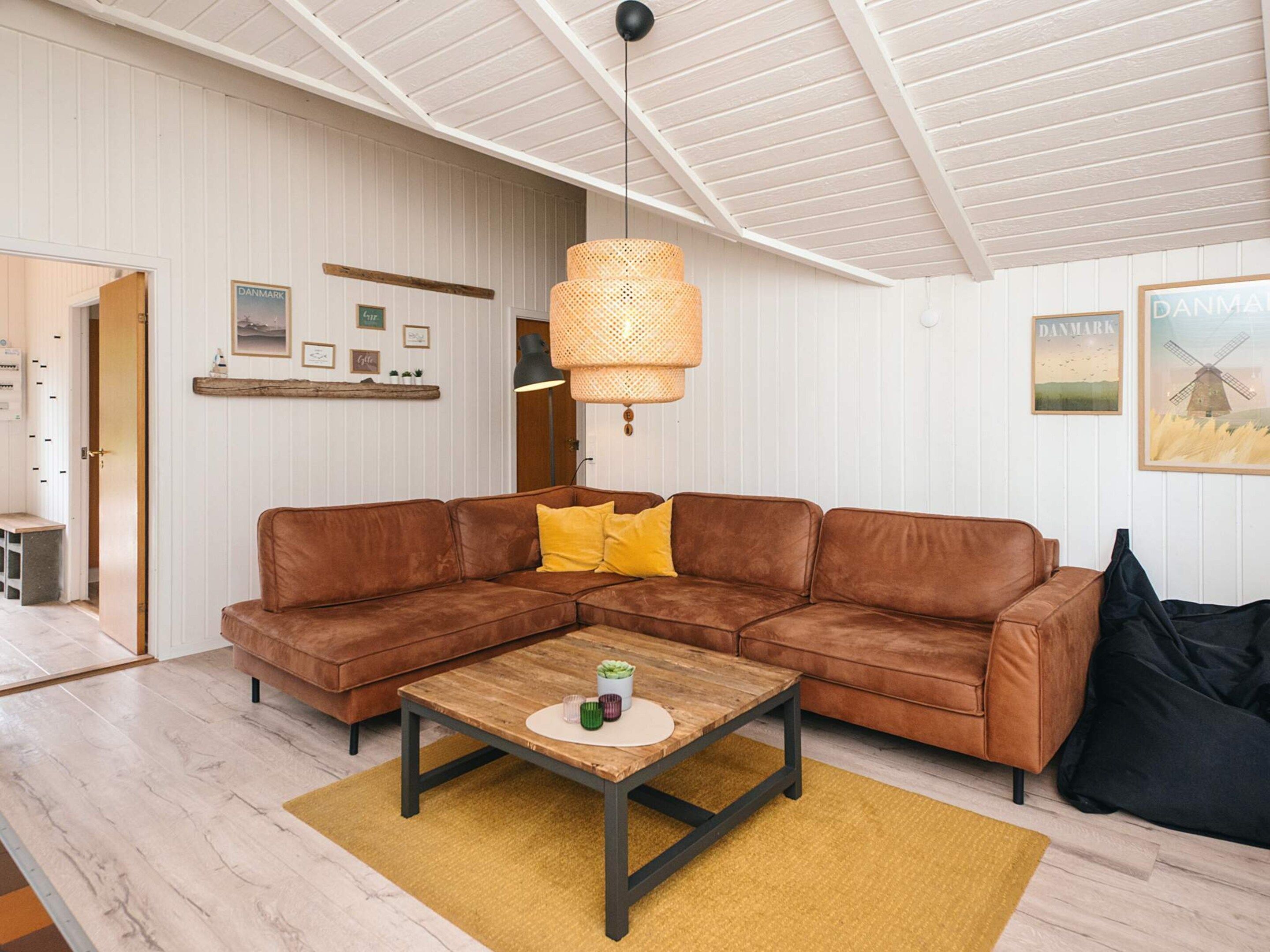 A living room with a brown leather sectional sofa, a wooden coffee table, a yellow rug, and a hanging wicker lamp.