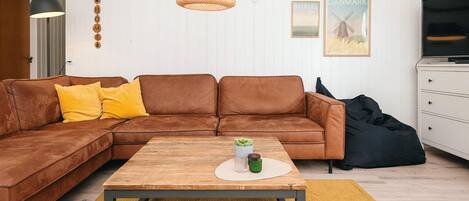 A living room with a brown leather sofa, a wooden coffee table, a black bean bag, a white cabinet, and a wall-mounted lamp.