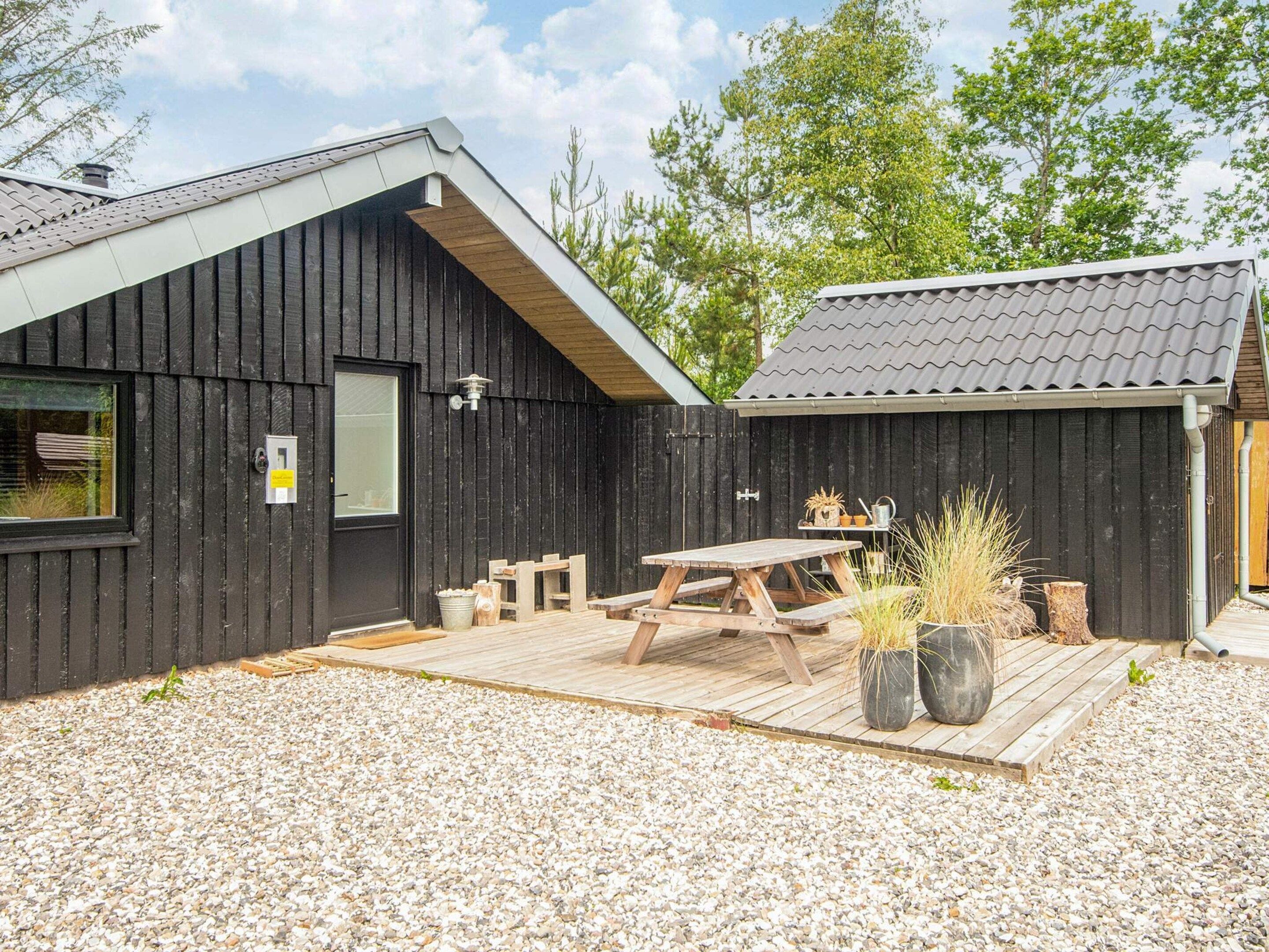 A wooden cabin with a sloped roof, a wooden deck, and a picnic table.