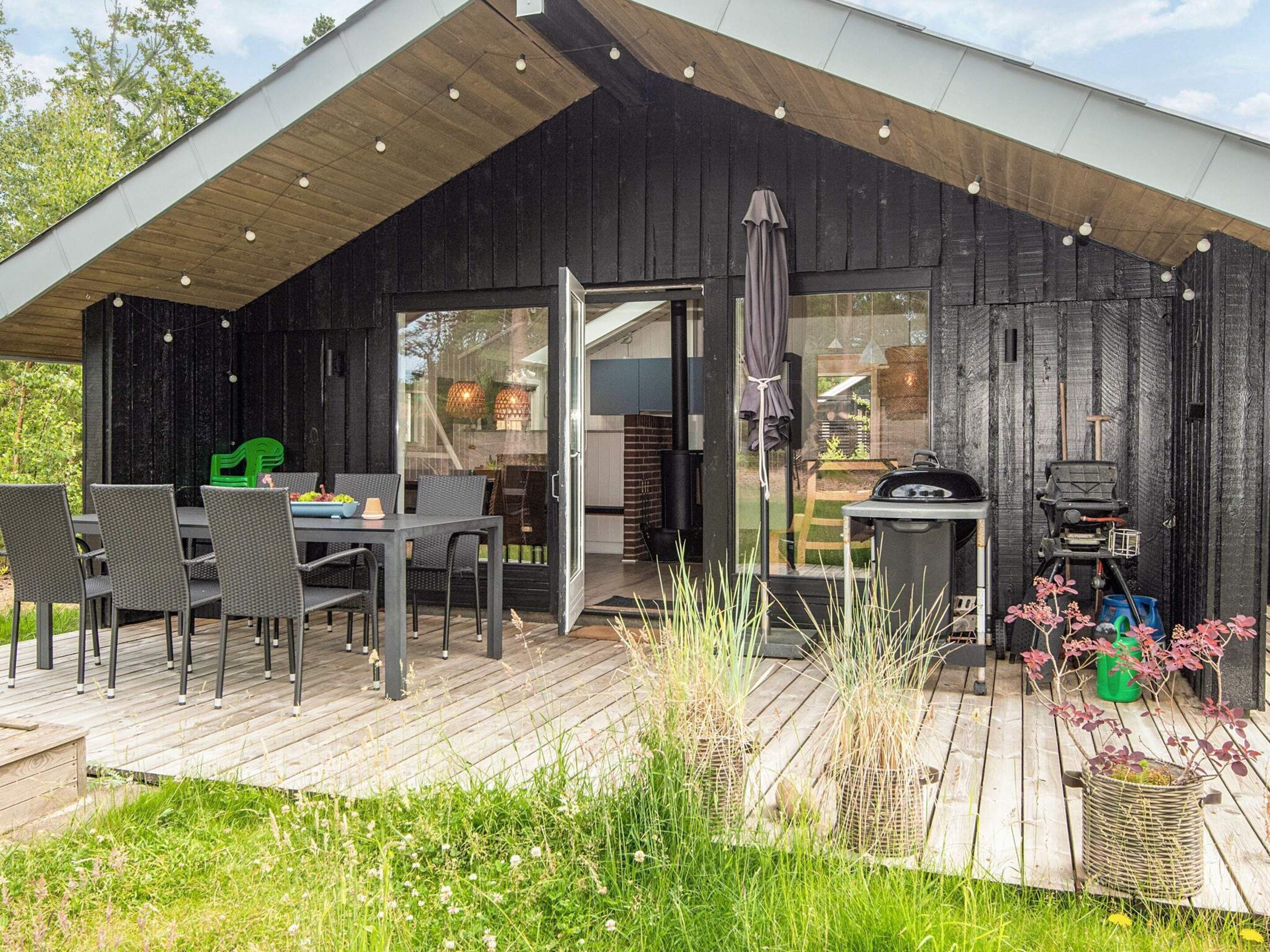 Ein modernes Haus mit einer großen Terrasse, einem Essbereich mit Stühlen und einem Tisch sowie einer Grillmöglichkeit.