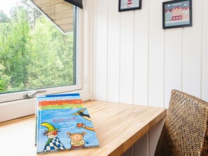 A window with a view of greenery, a wooden shelf with books, and a wicker chair.