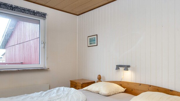 A bedroom with two single beds, a bedside table, a lamp, and a window with a view of a building. - 10 Person Holiday Home in Harboore (Harboore)