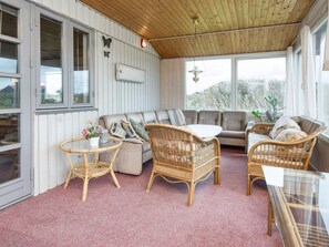 A cozy room with a wooden ceiling, a sofa, two wicker chairs, a small table, and a large window providing a view of the outdoors.