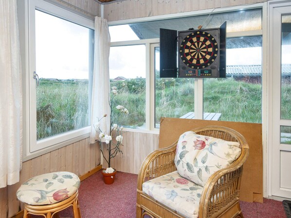 A room with a dartboard, wicker furniture, and a view of a grassy field.