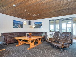 Une pièce avec un plafond en bois, une grande table en bois, un canapé en cuir marron et deux fauteuils en cuir.